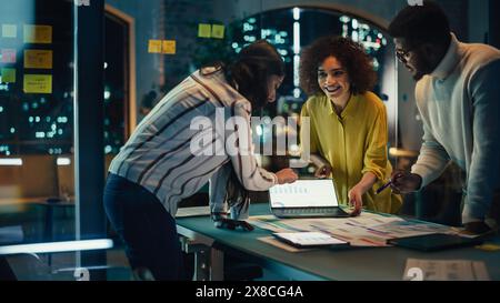 Multicultural Creative Colleagues Casually Joking, Discussing a New Business Opportunity, Talking in an Office Meeting Room, Using a Laptop and Tablet for Brainstorming Corporate Marketing Ideas. Stock Photo