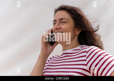 Radiating positive vibes, a middle-aged Caucasian woman with long hair is captured happily chatting on her mobile phone. Her striped blouse adds to th Stock Photo
