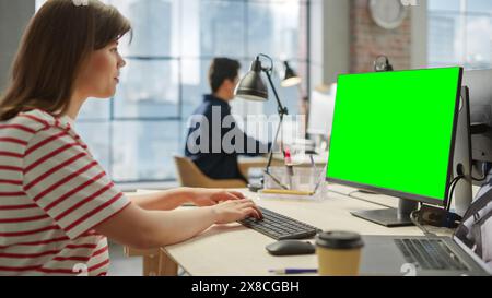 Portrait of White Young female Using a Computer with Green Screen Display in a Spacious Bright Office. Female Editor Using Chroma Key for Screen Replacement Using Editing Software. Stock Photo