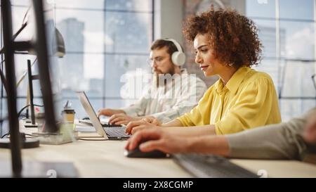 Portrait of Creative Biracial Woman Focused on Work While Using a Laptop in a Busy Office. Female Graphic Designer Studying Design Briefs and Making Notes. Stock Photo