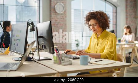 Biracial Woman Smiles Happily When Successfully Finishing a Work Project. Multiethnic Group of Creative Colleagues Working on Computers During Day in a Modern Bright Office. Stock Photo