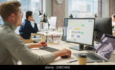 Portrait of Creative Young Man Consulting Using Computer and Laptop. White Male Supervisor Working on Scheduling Using Project Management Software. Stock Photo