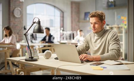 Portrait of Caucasian Man Focused on Work While Using Laptop in a Modern Spacious Office. Male Budget Analyst Reviewing and Developing Crisis Management Plan. Stock Photo