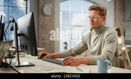 Portrait of focused Caucasian Young Male Working on Computer in a Modern Bright Office. Confident Human Resources Agent Answering and Collaborating Online with Colleagues. Stock Photo