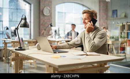 Diverse Multiethnic Creative Team Working On Computers in Bright Office. Portrait of Young Caucasian Man Using a Laptop and Smiling. Male Developer Collaborating with his Team Using a Smartphone. Stock Photo