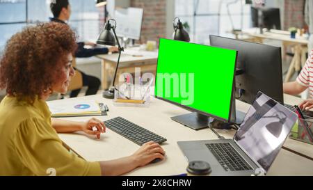High Angle View of a Female Worker Using Computer in a Bright Modern Office. Administrator Smiling and Preparing a Presentation Using Green Screen. Statistics and Charts are on Display on the Laptop. Stock Photo