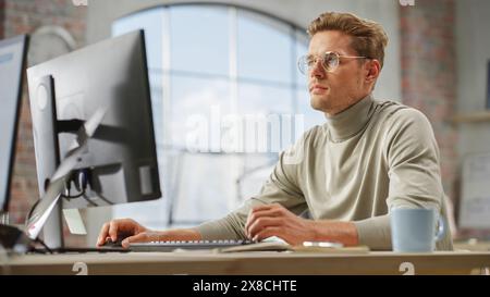 Portrait of a Young Handsome Man Working on a Computer in a Bright City Office. White Male Assistant Reviewing Documents for the Marketing Plan. Stock Photo