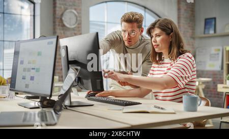 Two Creative Colleagues Discussing and Pointing at the Computer in Modern Bright Office. Caucasian Male Sales Manager Discussing Project Plan with White Female Legal Assistant. Stock Photo