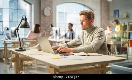 Portrait of White Focused man Using Laptop in a Contemporary Spacious Office. Account Specialist Focused While Having Productive Day. Active Colleagues Working on Computers in the Background. Stock Photo