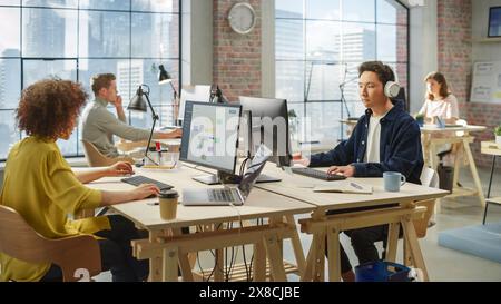 Multiethnic Creative Colleagues Working Using Computers in an Open Office During Day Time. Asian Man Listening to a Meeting on Headphones. Female Director working on a Schedule. Stock Photo