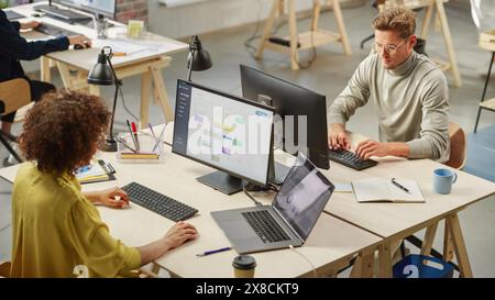 Group of Diverse Multiethnic Young Creative Colleagues Working On Computers in Modern Office. Biracial Female Team Lead Managing a Work Project that is Displayed on Screen. Young White Man Typing. Stock Photo