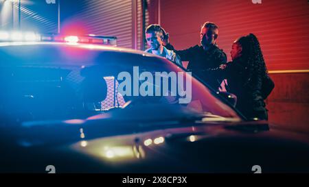 Two Police Officers Arrest Suspect, Put Him in Patrol Car. Officers of the Law Handcuff Dangerous Criminal on Dark City Street. Officers of the Law Arresting Felon, Fight Crime. Cinematic Stock Photo