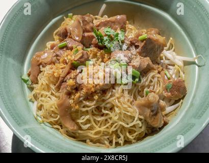 Egg Noodles with Braised pork (stewed pork) and Mung bean sprouts without Soup sprinkled with Coriander, Chopped onions and pepper in Green ceramic bo Stock Photo