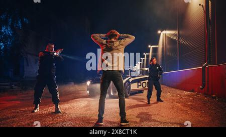 Two Police Officers Aim at a Fellon. Cops Using a Weapon to intimidate the Suspect. Fellon Raising Hands in Compliance. Heroic Law Enforcement Arresting a Dangerous Man. Symmetrical Shot Stock Photo