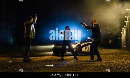 Two Police Officers in Pursuit of a Suspect. Cops Getting out of the Car Chase Criminal Through the Dark City Streets. Heroic Officers of the Law Arresting Felon. Intense Cinematic Stock Photo