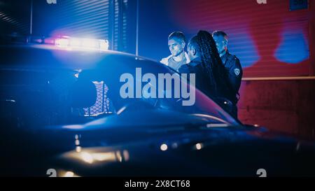 Two Police Officers Arrest Suspect, Put Him in Patrol Car. Officers of Law Handcuff Dangerous Criminal on City Street. Officers of the Law and Under Arrest Felon, Fight Crime. Cinematic Stock Photo