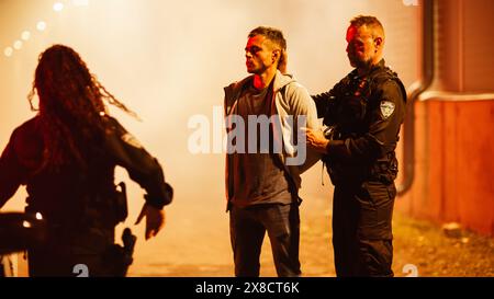 Two Police Officers Arresting a Criminal During Night and Putting Him in The Car. Female and Male Cops Effectively Imposing the Law, Taking a Cuffed Suspect to Police Station. Documentary Shot Stock Photo