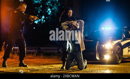 Black Female Police Officers Handcuffing a Compliant Suspect While her Male Partner Intimidats and Threatens the Criminal by Aiming a Gun at Him. Aesthetic Action Movie Shot Stock Photo