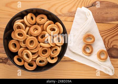 Several tasty bagels in a black ceramic plate on a wooden table, close-up, top view. Stock Photo