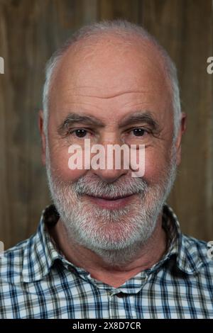 An older man with gray hair and a gray beard smiles warmly at the camera. Stock Photo