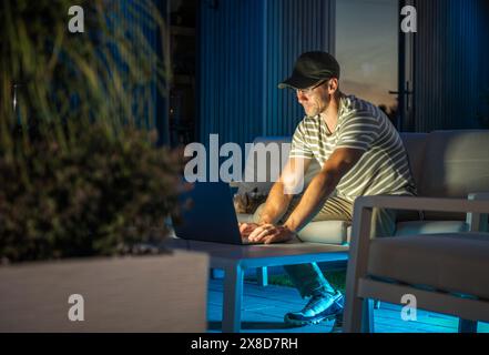 A man is seated on a couch indoors, engrossed in using a laptop computer. Stock Photo