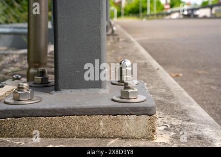 Close up of a pole on the street, screwed to the foundation of the pole, with shiny stainless steel bolts. More bolts along the line can be seen blurr Stock Photo