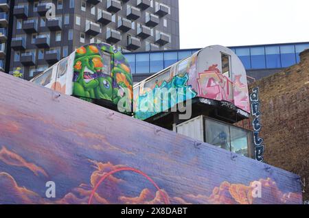 Famous landmark in hipster Shoreditch,  tube carriages suspended on an old railway viaduct, now trendy offices, over a street mural, east London, UK Stock Photo