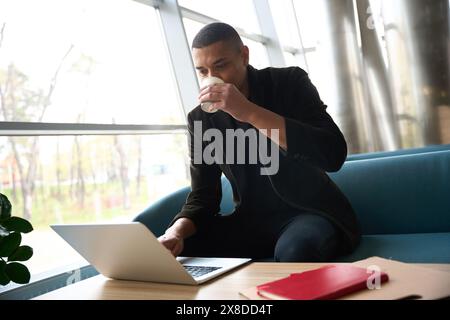 Young freelancer sitting and working on laptop while drinking coffee Stock Photo