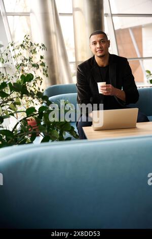 Young freelancer sitting on cozy couch and holding paper glass Stock Photo
