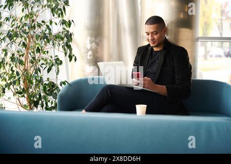 Smiling young freelancer sitting on couch and typing on smartphone Stock Photo