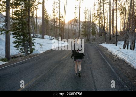 A female hiker walks down a road in Lassen Volcanic National Park in Northern California in winter. Stock Photo