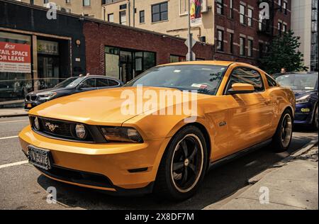 New York City, USA - August 05, 2023: 2011 Ford Mustang V6 yellow car front and driver side view, parked Stock Photo