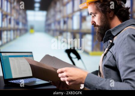 Industrial worker reading shipment invoice details in warehouse, supervising dispatch notes and order receipts in folder. Facility engineer working on supply chain management and quality control. Stock Photo