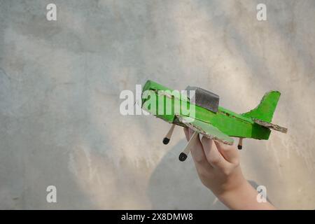 kid hand with green antique aircraft on grey wall background. Stock Photo