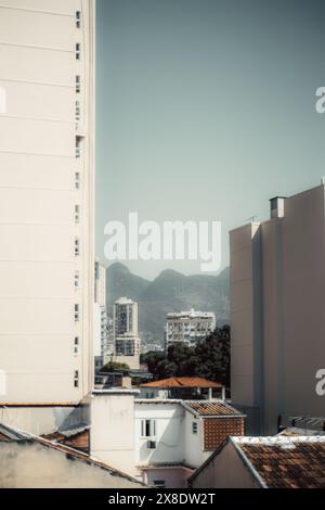 Urban cityscape of Rio de Janeiro featuring modern high-rise buildings framed between tall residential structures. Distant mountains provide a scenic Stock Photo