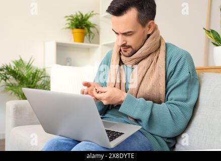 Ill young man taking pills while video chatting with doctor on laptop at home Stock Photo
