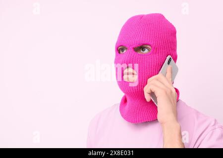 Handsome young man in balaclava talking by mobile phone on pink background Stock Photo