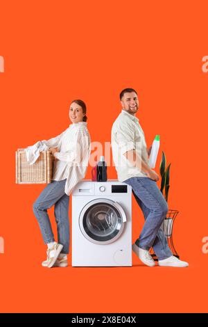 Young couple doing laundry on orange background Stock Photo