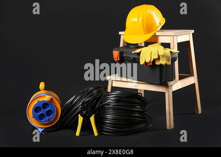 Stepladder with electrician tools, rolled cables and hardhat on black background Stock Photo
