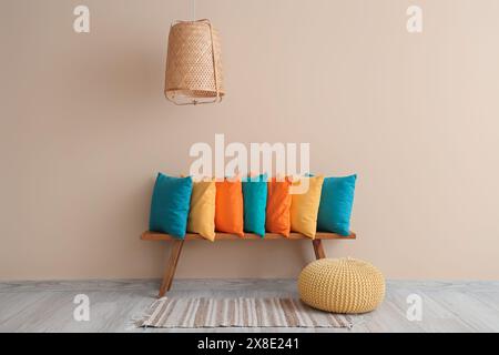 Colorful pillows on wooden bench and pouf near beige wall in room Stock Photo