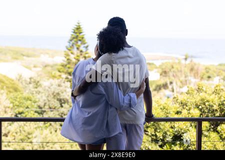A diverse couple embracing outdoors, enjoying ocean view Stock Photo