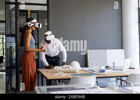 Colleagues in office using virtual reality headsets while working on project, copy space. African American male and indian female team leader examinin Stock Photo