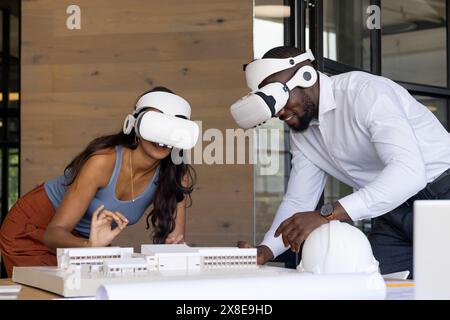 Diverse team of young colleagues using VR headsets for an architectural project. African American male and indian female examining building model on a Stock Photo