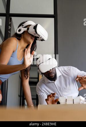 Diverse team using virtual reality headsets in modern office. Young African American male colleague and young indian female team leader interacting wi Stock Photo