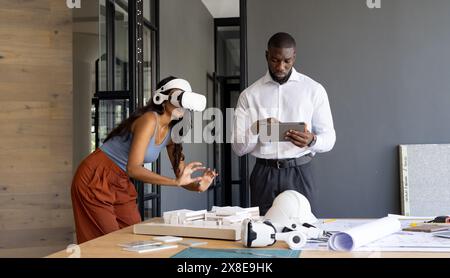 At modern office, diverse team working on architectural project. Young African American colleague using tablet while young Indian team leader explorin Stock Photo