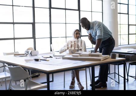 At modern office, diverse team working on architectural project, copy space. African American male colleague and Indian female team leader discussing Stock Photo
