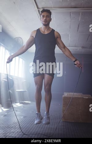 At gym, young biracial man gym-goer jumping rope, looking strong and fit Stock Photo