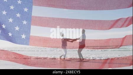 Diverse couple holding hands on beach, American flag overlaying Stock Photo