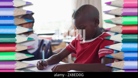 In school, African American boy/student wearing red shirt focusing on writing Stock Photo