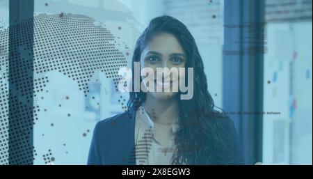 Image of rotating globe and computer language over laughing biracial woman standing in office Stock Photo